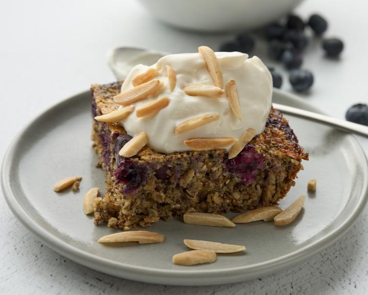 A slice of blueberry baked oatmeal with whipped topping and almonds.