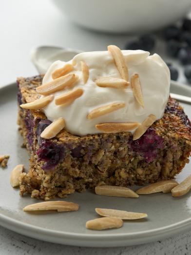 A slice of blueberry baked oatmeal with whipped topping and almonds.