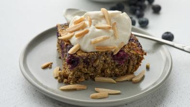 A slice of blueberry baked oatmeal with whipped topping and almonds.