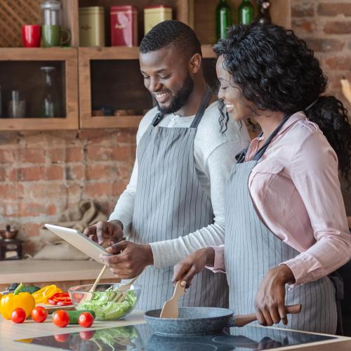 A couple cook together in a kitchen while watching a diabetes-friendly cooking class on their tablet