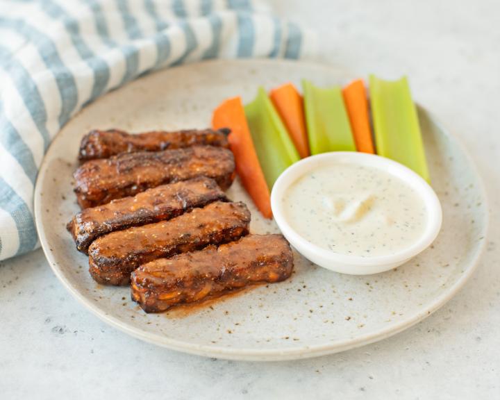 Buffalo Tempeh Wings on plate with celery and carrots and dipping sauce