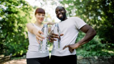 Smiling couple out for a jog in park holding water bottles