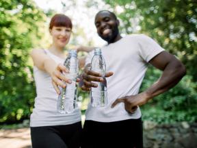 Smiling couple out for a jog in park holding water bottles
