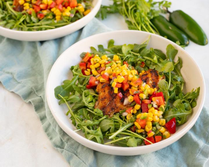 A bowl of grilled tilapia on a salad of arugula and corn for a heart and diabetes healthy dash diet