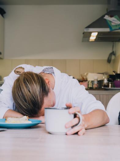 Tired Woman next to Child eating an orange at a table in the kitchen.