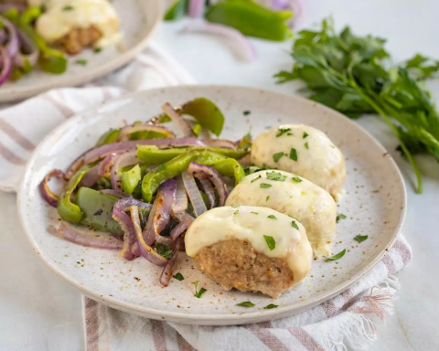 Turkey meatloaf on a plate with sauteed peppers and onions.