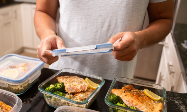 A pair of hands add a lid to meal prepped dinners