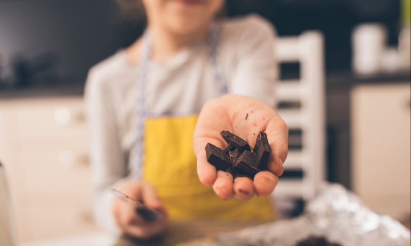 A person cutting up dark chocolate and offering it towards the camera